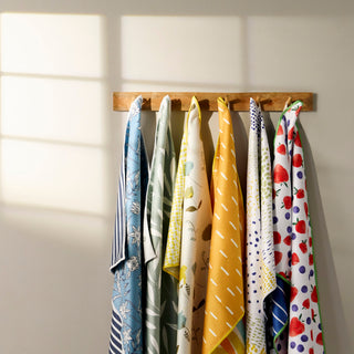 Set of colorful kitchen towels hanging on a wooden rack against a neutral wall.