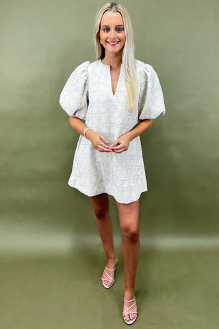 Woman wearing a white patterned dress against a green background