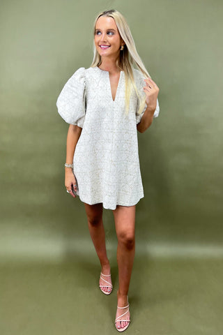 Woman wearing a light-colored dress with puff sleeves against a green background