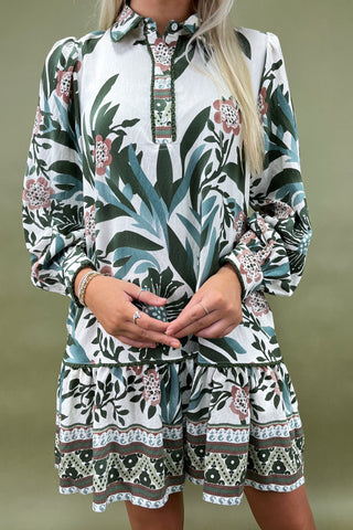 Woman wearing a long-sleeve dress with a floral and leaf pattern on a plain background