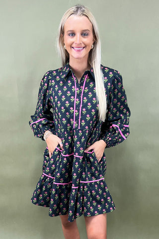 Woman wearing a black floral dress with pink accents against a green background