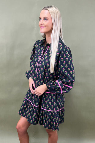 Woman wearing a dark floral dress with pink accents against a plain background