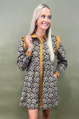 Woman wearing a floral dress with mustard yellow accents against a green background