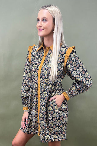 Woman wearing a floral dress with yellow trim against a green background