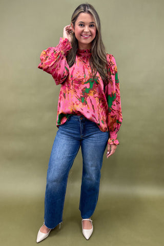 Woman wearing a pink floral blouse and blue jeans against a green background