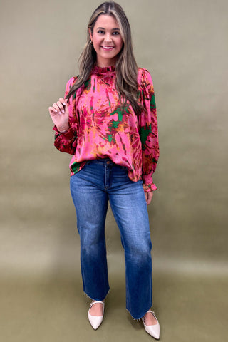 Woman wearing a pink floral blouse and blue jeans against a beige background