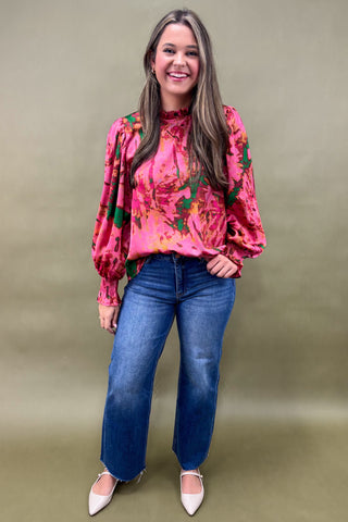 Woman wearing a pink floral blouse and blue jeans against a green background