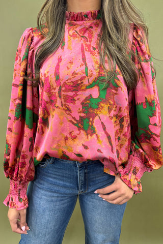 Person wearing a vibrant pink floral blouse with blue jeans on a green background