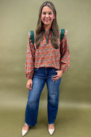 Woman wearing a floral blouse and blue jeans against a green background