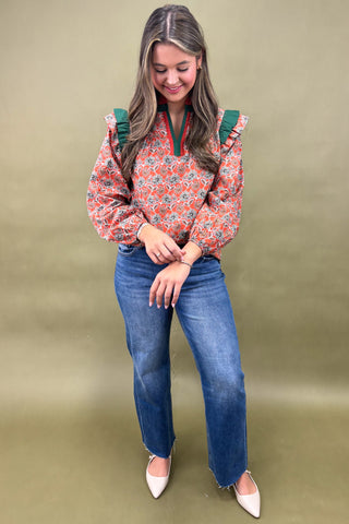 Woman wearing a floral blouse and blue jeans against a green background