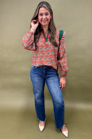 Woman wearing a floral blouse and blue jeans against a green background
