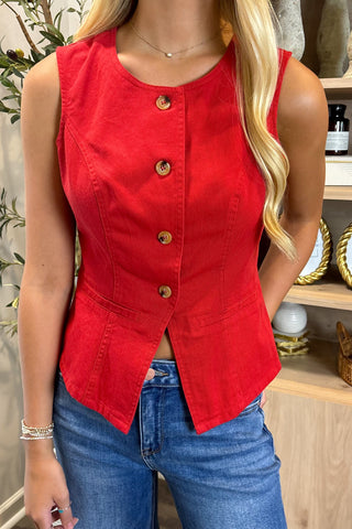 Person wearing a red sleeveless button-up top with blue jeans in an indoor setting.