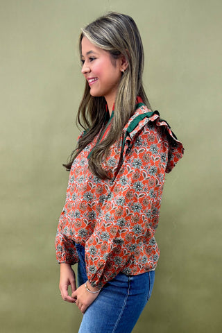 Woman wearing a floral blouse with ruffled sleeves against a green background