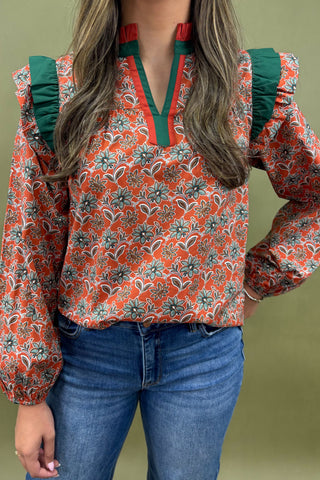 Person wearing a floral patterned blouse with green accents and blue jeans on a plain background