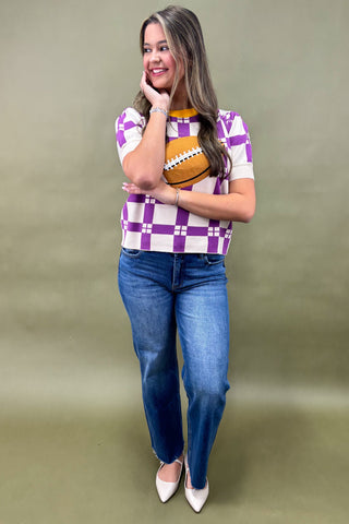Woman wearing a checkered shirt and jeans, holding a football against a plain background