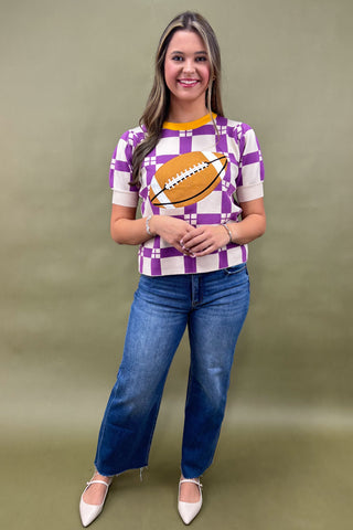 Woman wearing a checkered shirt with a football design and blue jeans on a green background