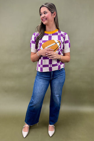 Woman wearing a checkered shirt with a football design and blue jeans on a green background
