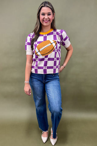 Woman wearing a checkered shirt with a football design and blue jeans on a plain background