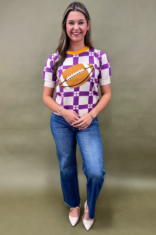 Woman wearing a purple checkered shirt with a football design and blue jeans on a plain background