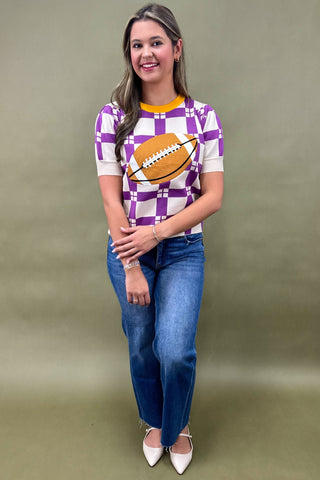 Woman wearing a checkered shirt with a football graphic and blue jeans against a plain background