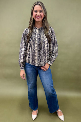 Woman wearing a patterned blouse and blue jeans against an olive green background