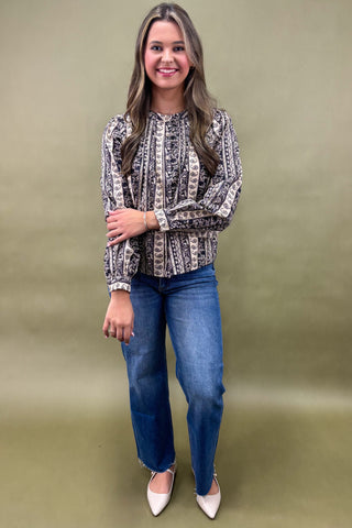 Woman wearing a patterned blouse and blue jeans against a green background