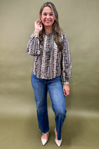 Woman wearing a patterned blouse and blue jeans against a green background