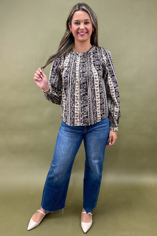 Woman wearing a patterned blouse and blue jeans against a green background