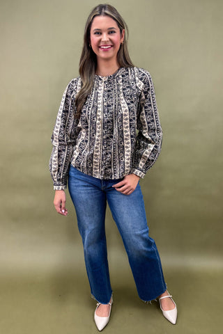 Woman wearing a patterned blouse and blue jeans against an olive green background