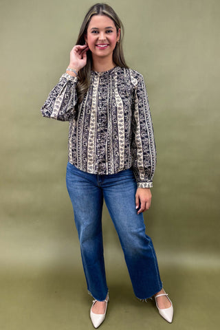 Woman wearing a patterned blouse and blue jeans against an olive green background