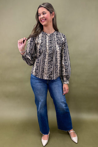 Woman wearing a patterned blouse and blue jeans against a green background