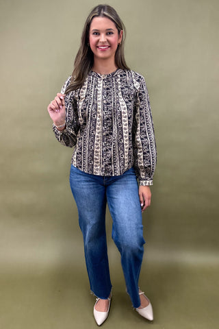 Woman wearing a patterned blouse and blue jeans against a green background