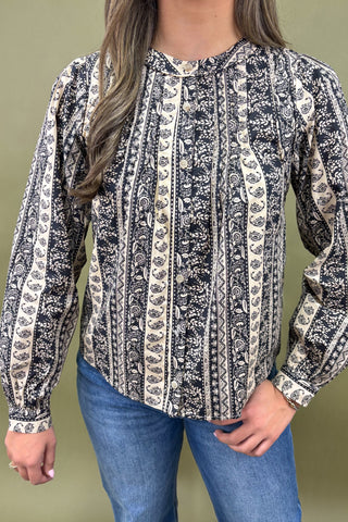 Person wearing a long-sleeve patterned shirt with blue jeans against a green background