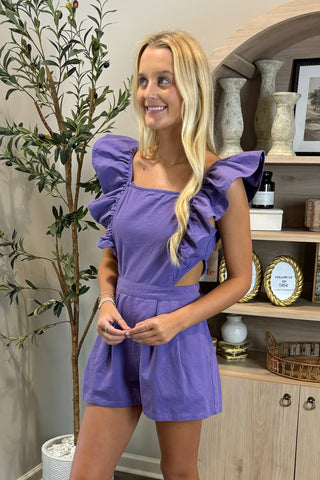 Woman wearing a purple outfit standing in a room with decor elements.