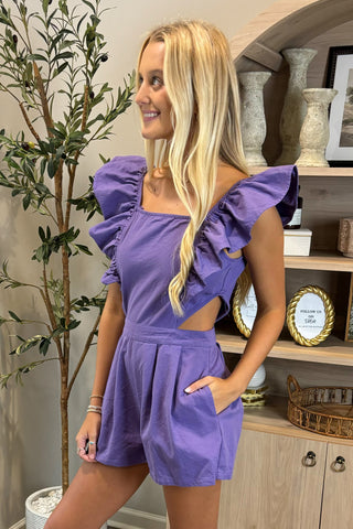 Woman wearing a purple dress standing in a room with decorative items.