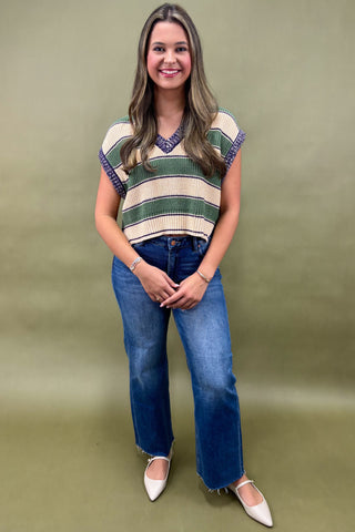 Woman wearing a striped sweater and blue jeans against a green background