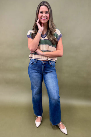 Woman wearing a striped shirt and blue jeans against a green background