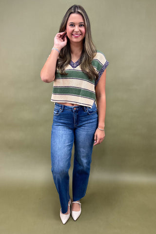 Woman wearing a striped top and blue jeans against a green background