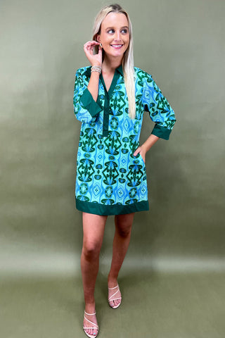 Woman wearing a green and blue patterned dress against a plain background