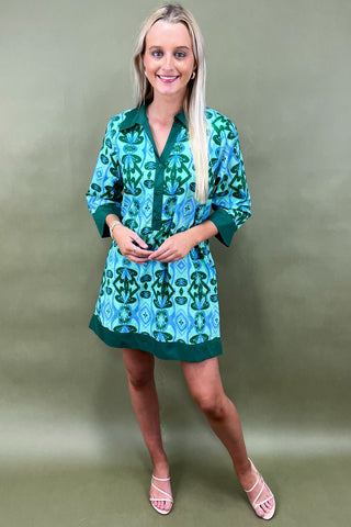 Woman wearing a green and blue patterned dress against a plain background