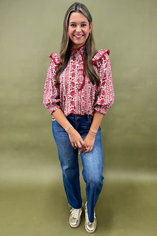 Woman wearing a red patterned blouse and blue jeans on a green background
