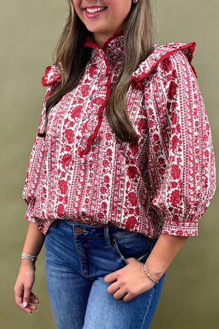 Woman wearing a red and white patterned blouse with blue jeans against a green background