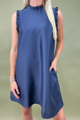 Woman wearing a blue dress with ruffled neckline against a green background