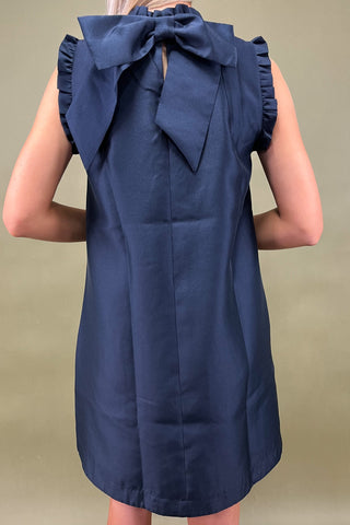 Navy blue dress with a large bow detail on the back against a beige background