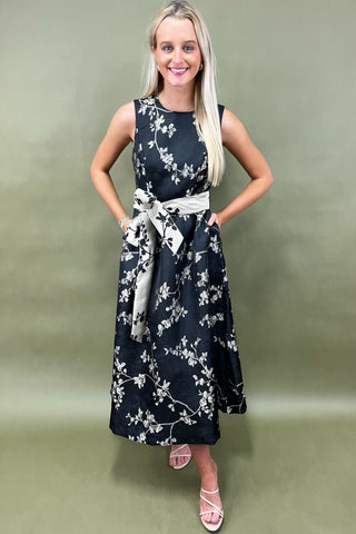 Woman wearing a black floral dress with a white belt against a green background