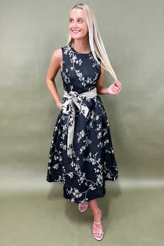 Woman wearing a black floral dress with a white belt against a plain background