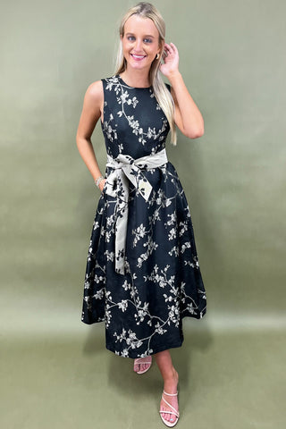 Woman wearing a black floral dress with a white belt against a green background