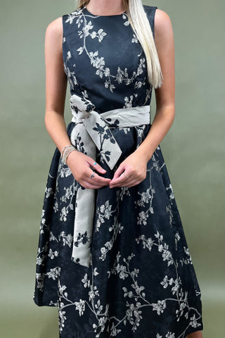 Woman wearing a navy floral dress with a white scarf, against a plain background