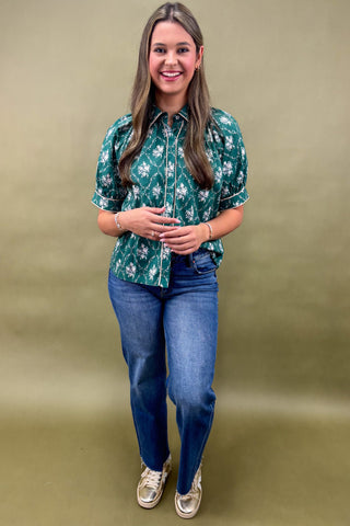 Woman wearing a green floral blouse and blue jeans against a beige background