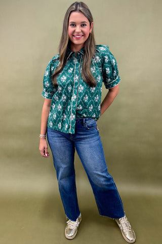Woman wearing a green floral blouse and blue jeans against a green background